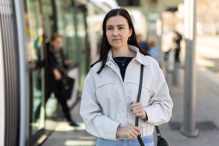 Woman is waiting for tram at stop of urban transport with spring day