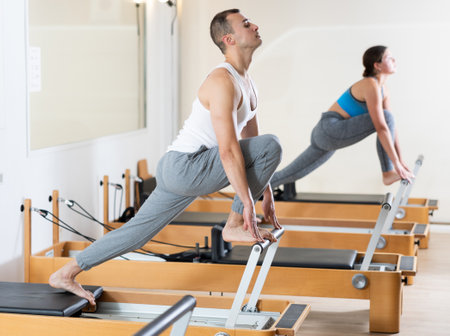 Sporty man in sports wear engages in Pilates on reformer machineの写真素材