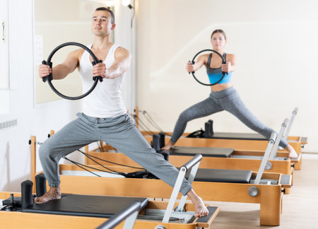 Girl and man exercising with pilates rings on reformer in fitness studio. Healthy lifestyle conceptの写真素材