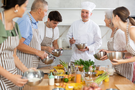 Cheerful middle-aged man chef of cooking course teaching attendees how to mix sauceの写真素材