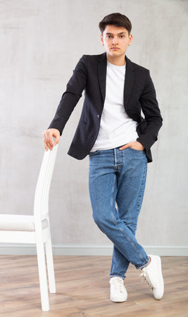 Confident young man standing next to chair in the middle of the roomの写真素材