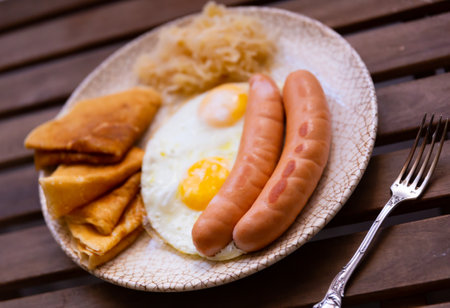 Fried sausages with scrambled eggs, pancakes and cabbage on a wooden backgroundの写真素材