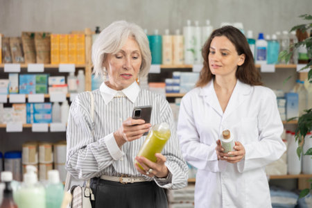 Mature woman in pharmacy scans QR code on shampoo, woman pharmacist in backgroundのeditorial素材