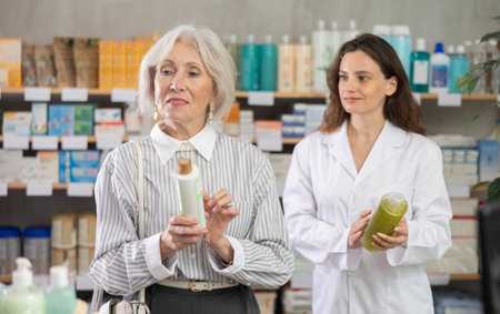 Mature woman choose shampoo, woman pharmacist offers similar itemの写真素材