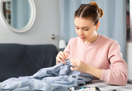 Young woman sewing on button at home