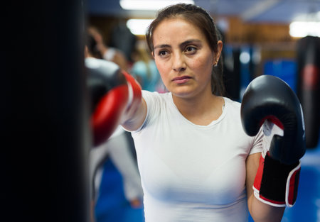 Young Latina in boxing gloves mastering punches on punching bagの写真素材