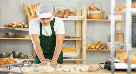 Young male baker kneads the dough in bakeryの写真素材