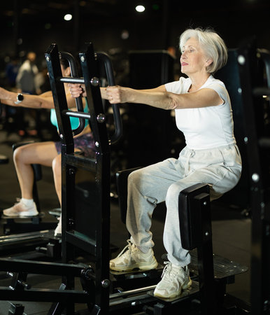 Elderly woman using standing abductor machine during workout at gym