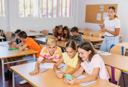 Schoolchildren use mobile phones at the lesson in classroom
