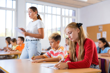 Interested diligent preteen schoolgirl writing exercises at lessons