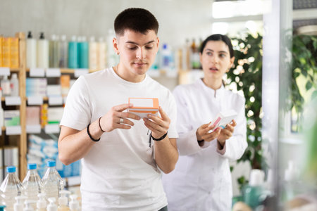 Young man buys pills at drug store, pharmacist in backgroundの写真素材