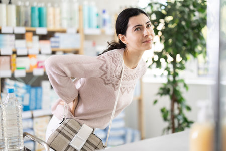 Girl suffers from back pain - looks for medicine in modern pharmacy