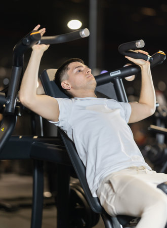 During training session in mini group of athletes, man exercises on shoulder press machine