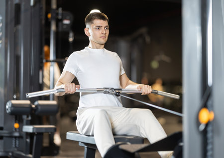In gym, young man uses cable row machine to strengthen arm muscles