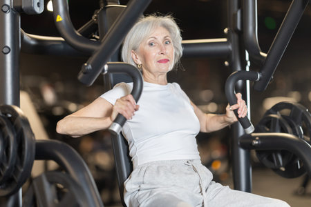 In gym, senior woman uses chest press machine to strengthen arm muscles