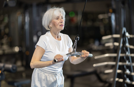 In gym, senior woman uses cable row machine to strengthen muscles.