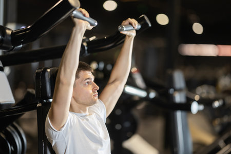 Young man training on shoulder press machine in gymの写真素材