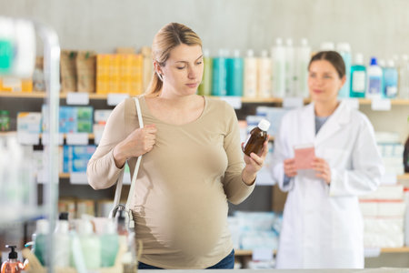 Pregnant woman choosing herbal syrup in local pharmacyの写真素材