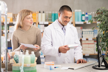 Man pharmacist is working at computer, communicate with girl customerの写真素材