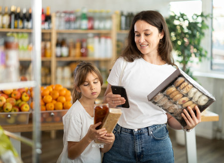Girl with mother customers at shop scans QR code on sweets package using phone cameraの写真素材