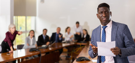 Dissatisfied businessman reads a document against the background of a team of businessmen in meeting roomの写真素材