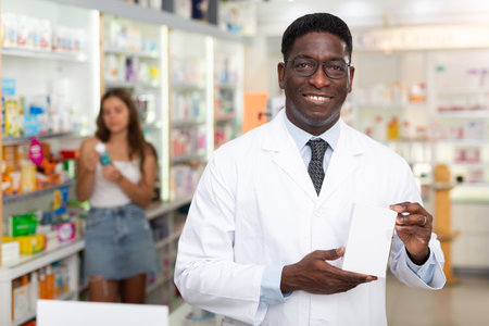 Portrait of african american male pharmacist in pharmacy demonstrating goodsの写真素材