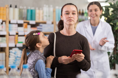 Woman and girl in pharmacy with phone, pharmacist in backgroundの写真素材