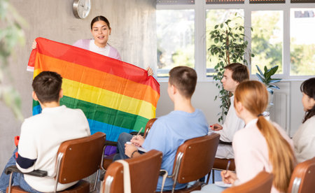 Students at lesson with classmates, listening mature teacher talking about LGBT community and showing rainbow flagの写真素材