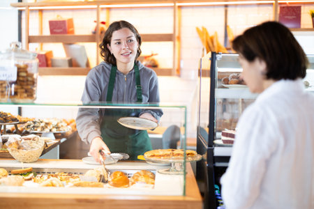 Saleswoman in an apron offers a buyer pastriesの写真素材