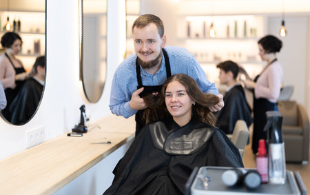 Young man barbershop employee stands next to female client, discussing details of haircutの写真素材