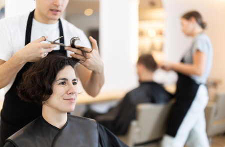 Young man barbershop employee stands next to female client, discussing details of haircutの写真素材