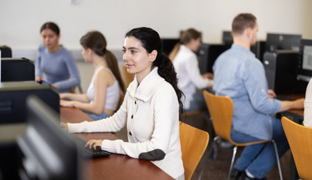 Girl student of computer courses looks at monitor screen, types on keyboard and does work