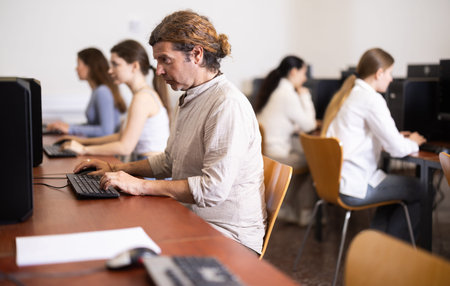 Side view on male student sitting at desk with pc, preparing for exam in computer class