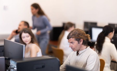 Side view on male student sitting at library desk with pc, preparing for exam