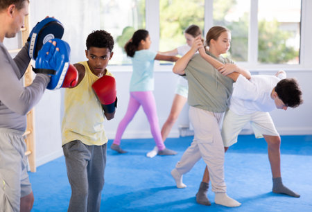 African american boy in boxing gloves practicing punches on mitts with coach