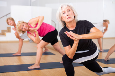 Aged woman practicing Parvritta Parsvakonasana during group yoga trainingの写真素材