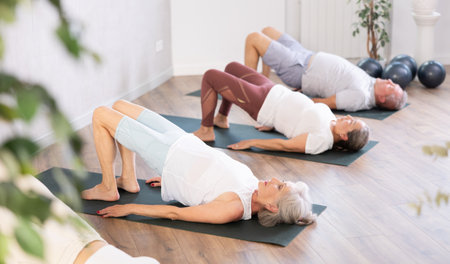 Elderly woman in company of hatha yoga lovers performs bridge pose, setu bandha sarvangasanaの写真素材