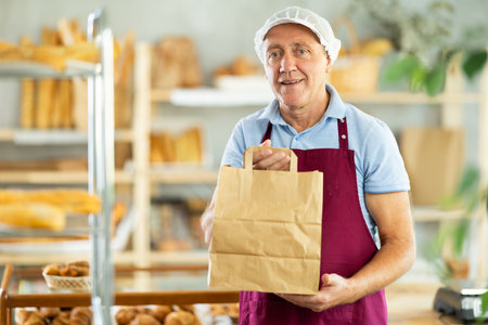 Elderly man seller with paper bags in bakeryの写真素材