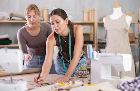 Two young female dressmakers drawing on paper in sewing workshopの写真素材