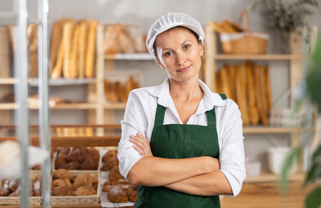 Woman baker in white coat overall and cap stands in trading hall of bakeryの写真素材