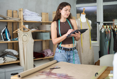 Young female dressmaker drawing in tablet in sewing workshopの写真素材