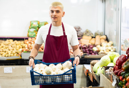 Man salesperson carries large basket of daikon radish from warehouse to sales area in shopの写真素材