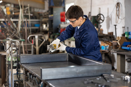 Young guy polishing metal part in workshopの写真素材
