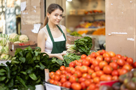 Young woman seller puts spinach in vegetable shopの写真素材