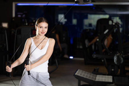 Active athlete young woman during exercises on crossover exercise machine with loops and weighting