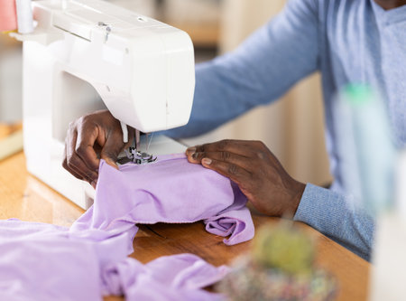 African American man tailor sews clothes in sewing machine, close upの写真素材