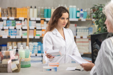 Woman employee at counter with computer sells pills and ointments to customerの写真素材