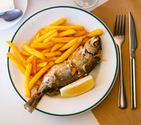 Baked salema porgy with fried potatoes and lemonの写真素材