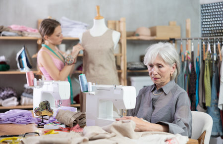 Elderly woman sews on machine female assistant sews on mannequin