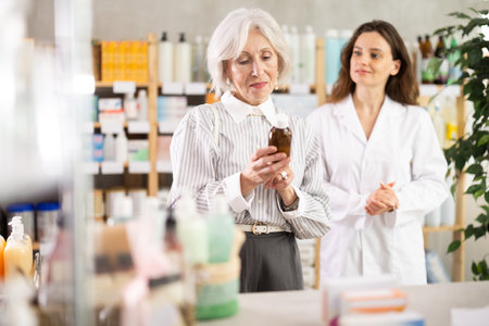 Mature woman choose antitussive syrup, woman pharmacist offers similar itemの写真素材